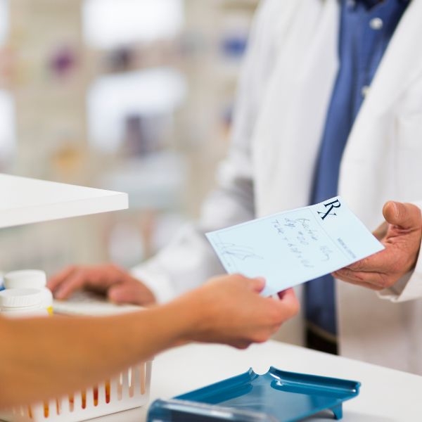 person handing a prescription for a medicine to a pharmacist